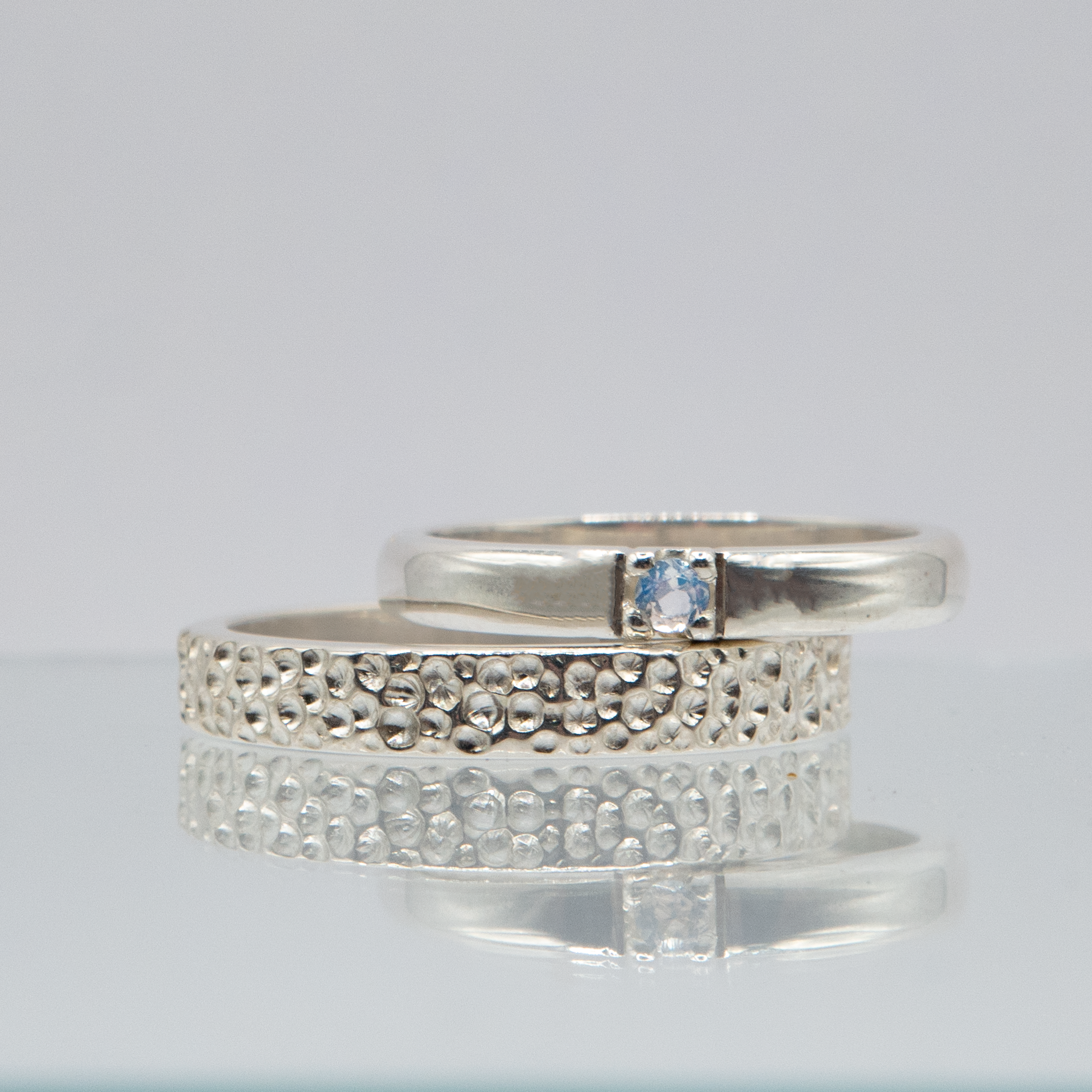 Handgemaakte trouwringen van zilver met maansteen in de vrouwenring en maanoppervlak afwerking in de herenring.